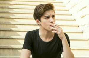 the guy is a teenager with a cigarette outdoors